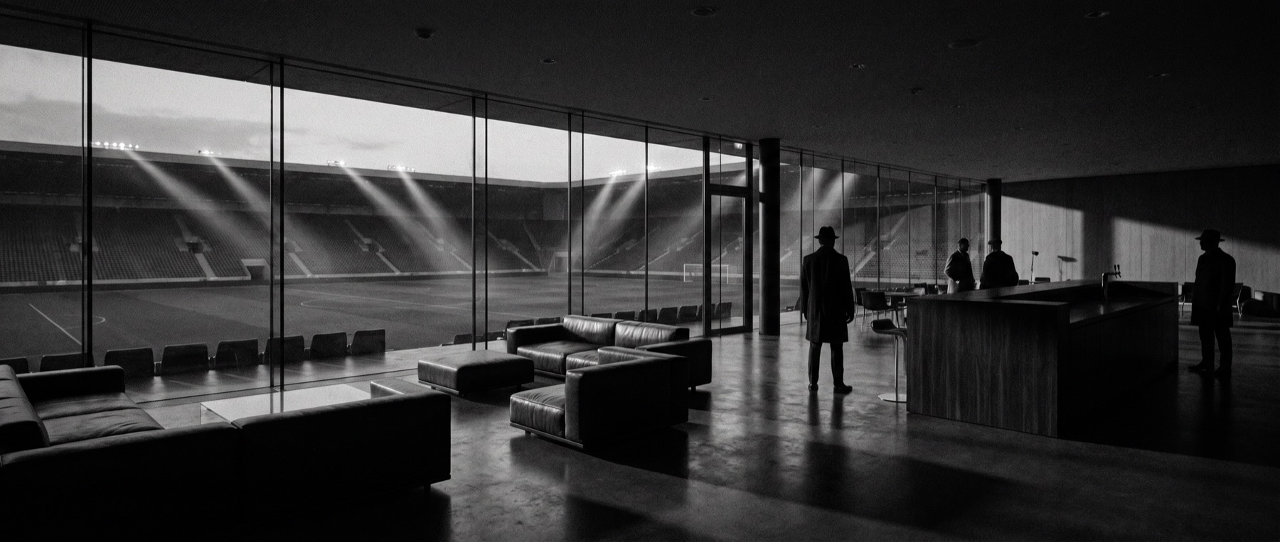 Executive lounge de un estadio de fútbol con vistas al terreno de juego al atardecer, tratamiento en blanco y negro